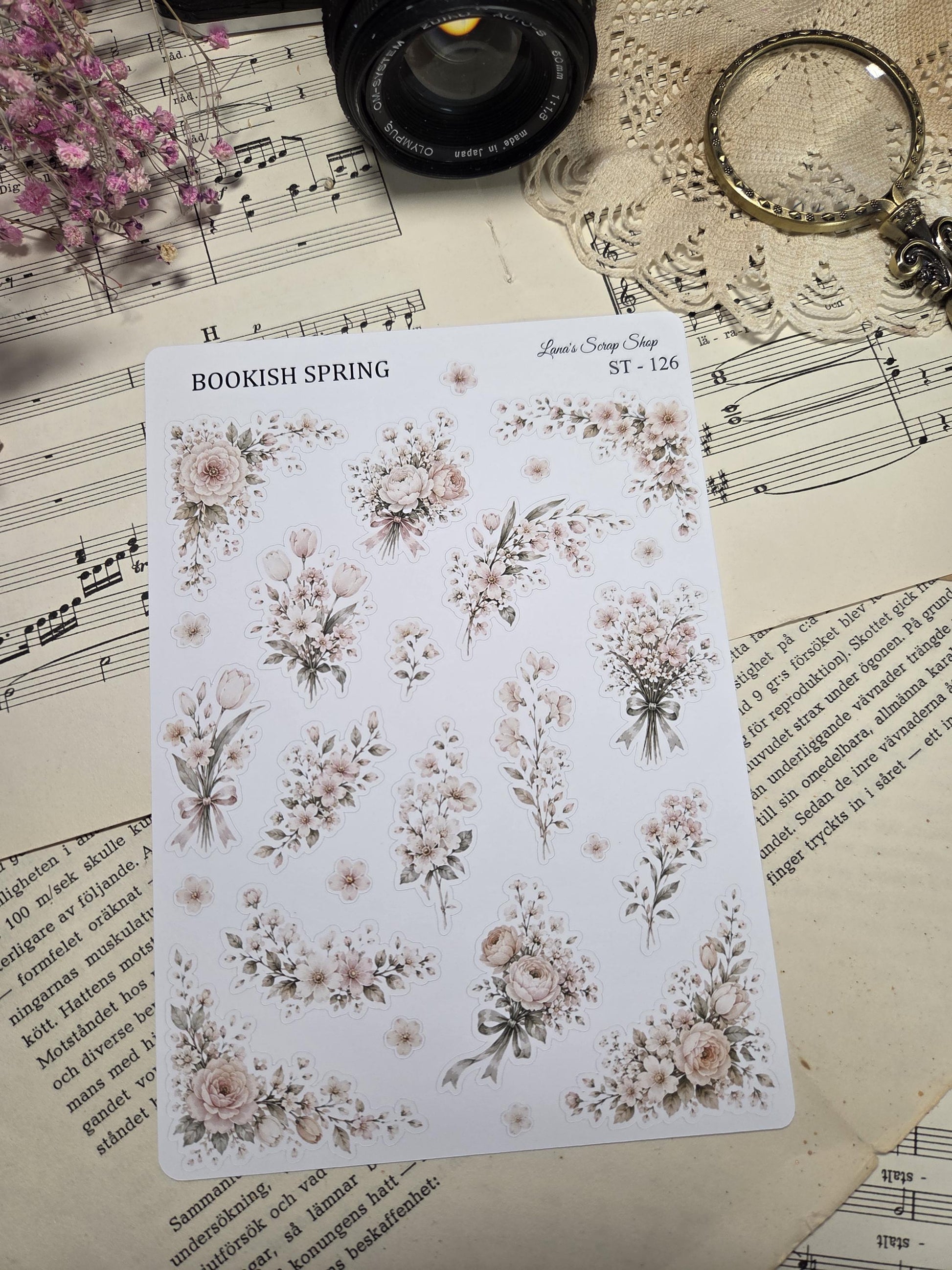 A sticker sheet of floral stickers with the text "BOOKISH SPRING" and "Lana's Scrap Shop ST-126". The stickers feature bouquets and floral arrangements in cream, beige, and light pink, with green leaves and ribbons.