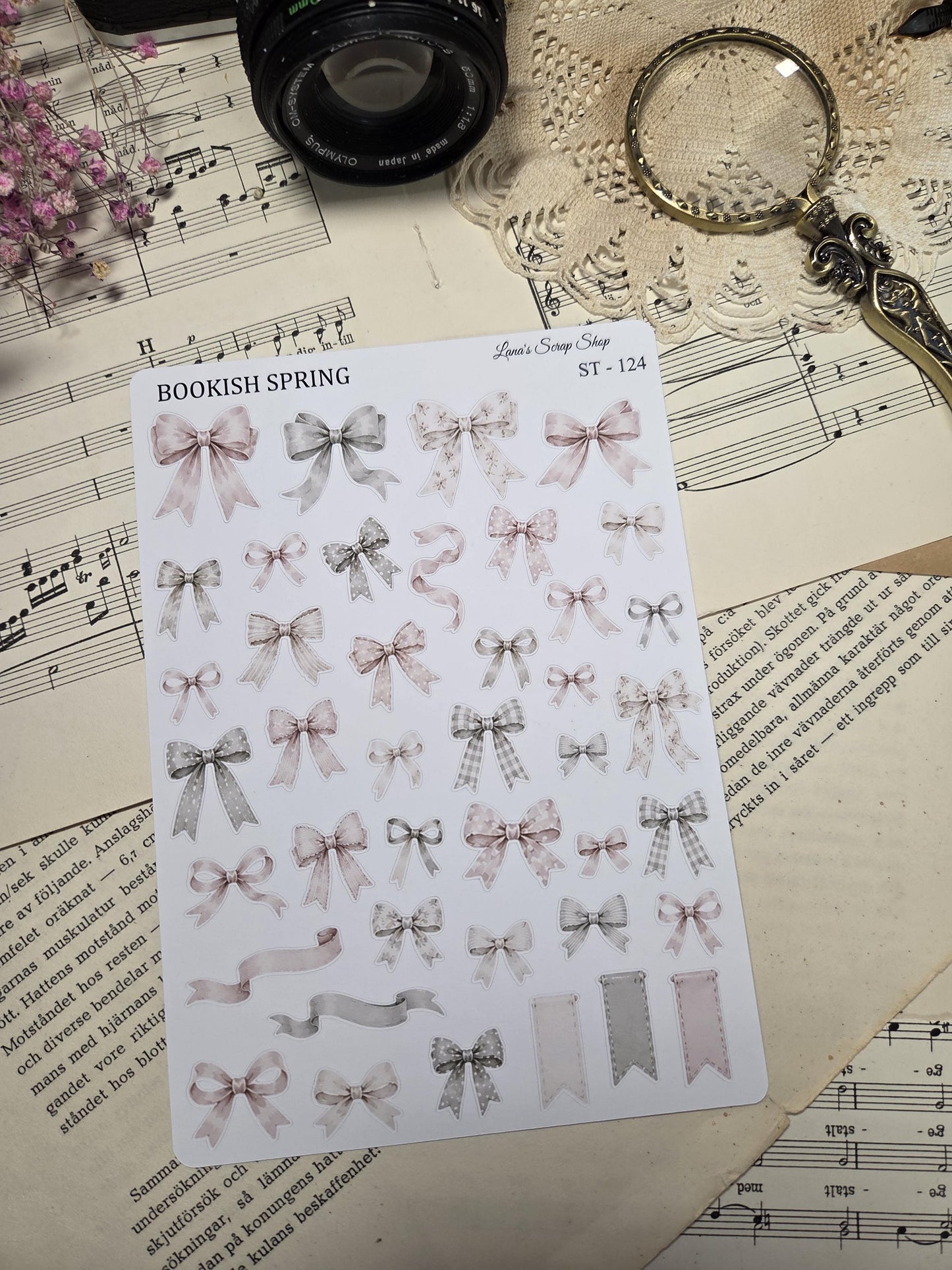 A sticker sheet with assorted bows in pastel pink, grey, and white. The bows have polka dots, gingham, and plain designs. The text "BOOKISH SPRING" is printed on the sheet.